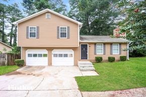 Lithonia house for rent - A house with a brown siding and a black door is surrounded by greenery.