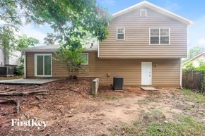 Lithonia house for rent - A house with a brown siding and a white door is surrounded by trees and has a dirt area in front.