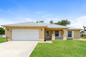 Cape Coral house for rent - a yellow house with a white garage door and a lawn