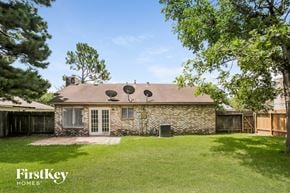 Katy house for rent - a backyard with a stone house and a yard with grass and trees