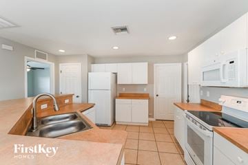 Cape Coral house for rent - a kitchen with white cabinets and appliances and a sink