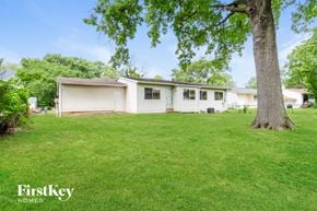 Florissant house for rent - A tree stands in a grassy yard in front of a white house.