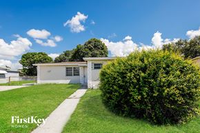 Miami Gardens house for rent - A white house with a green lawn and a bush in front.