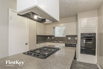 Spring house for rent - a kitchen with white cabinets and granite counter tops and a stove top oven