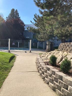 Boise apartment for rent - A concrete walkway leads to a metal fence and a building.