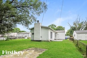 Florissant house for rent - A small house with a metal roof is surrounded by a grassy area and other similar houses.