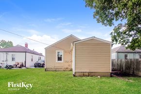 Indianapolis house for rent - A beige house with a brown roof is in the foreground of a grassy area.