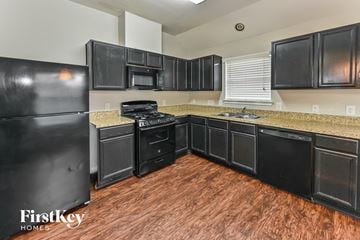 Houston house for rent - a kitchen with black cabinets and black appliances and a wooden floor