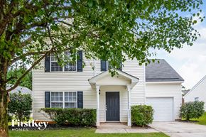 Charlotte house for rent - A white house with a black door and windows is surrounded by greenery.