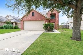 Houston house for rent - A red brick house with a white garage door and a tree in front.