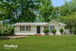 Adamsville house for rent - A white house with a black door and red window frames is surrounded by greenery.
