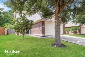 Houston house for rent - A tree stands in a grassy front yard in front of a house.