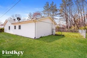 Indianapolis house for rent - A small white house with a metal roof and a satellite dish on the roof is surrounded by a grassy lawn and trees.