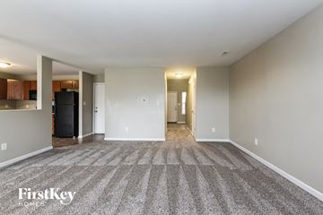 Indianapolis house for rent - A spacious room with a carpeted floor and a kitchen area in the background.