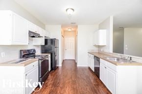 North Port house for rent - a kitchen with white cabinets and black appliances and a wood floor
