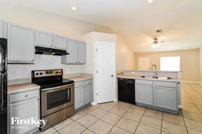 Deltona house for rent - a kitchen with white cabinets and stainless steel appliances and tiled floors