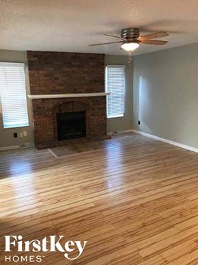 Blue Springs house for rent - an empty living room with wood floors and a brick fireplace