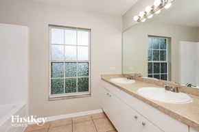 Lehigh Acres house for rent - A bathroom with a large mirror, two sinks, and a window with a view of trees.