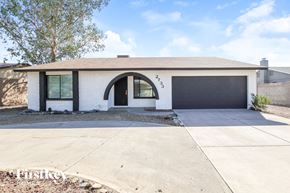 Phoenix house for rent - A white house with a black garage door and a black arched doorway.