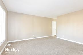 Florissant house for rent - A spacious room with a carpeted floor and a door on the right side.