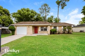 Deltona house for rent - A house with a red door and a brown roof is surrounded by green grass and trees.