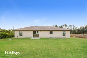 Lehigh Acres house for rent - A small house with a brown roof and a white front door is surrounded by a grassy lawn.