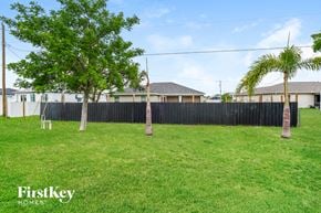 Cape Coral house for rent - A grassy area with trees and a fence, with the words "FirstKey Homes" on the bottom left.