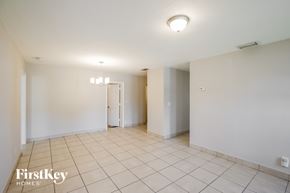 Miami Gardens house for rent - A spacious room with white walls and tile flooring, featuring a chandelier and a doorway leading to another room.