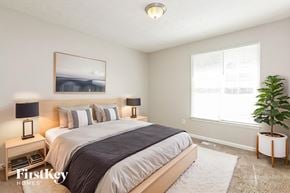Powder Springs house for rent - A bedroom with a large bed, a nightstand with a lamp, a framed picture on the wall, and a potted plant on the side table.