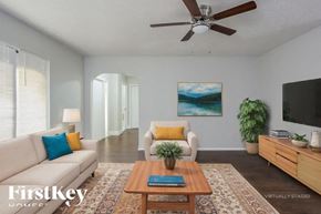 Cape Coral house for rent - A living room with a couch, a chair, a coffee table, a plant, a painting, a ceiling fan, and a flat screen TV.