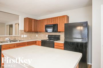 Dallas house for rent - a kitchen with wood cabinets and black appliances and a white counter top