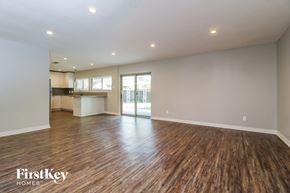 Plano house for rent - A spacious room with wooden flooring and a kitchen area in the background.