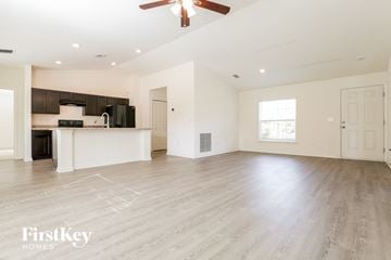 North Port house for rent - A spacious living room with a kitchen in the background and a ceiling fan above.