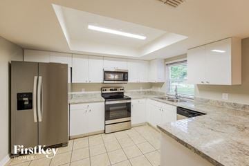 Cape Coral house for rent - a large kitchen with white cabinets and stainless steel appliances