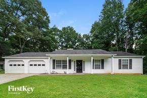 Douglasville house for rent - A white house with a black door and windows is surrounded by trees.