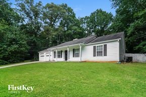 Douglasville house for rent - A white house with a grey roof is surrounded by greenery.