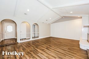 Fort Worth house for rent - A spacious room with wooden floors and white walls, featuring a white door with a diamond pattern and three arched windows.