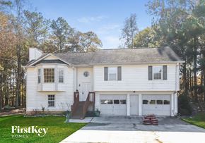 Powder Springs house for rent - A white house with a garage is surrounded by trees.