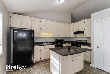 Powder Springs house for rent - A kitchen with a black fridge and white cabinets.