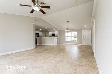 Lehigh Acres house for rent - A spacious room with a fan and a kitchen in the background.