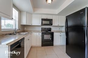 Lehigh Acres house for rent - a kitchen with white cabinets and black appliances