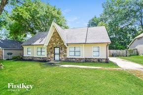 Memphis house for rent - A house with a stone wall and a brown roof is surrounded by a grassy lawn.