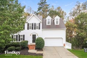 Greensboro house for rent - A white house with a black door and windows is surrounded by greenery.