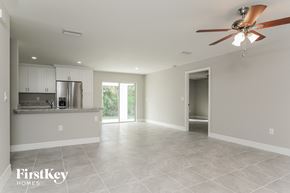 Lehigh Acres house for rent - an empty living room with a kitchen and a ceiling fan