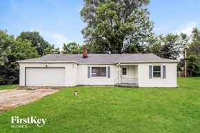 Indianapolis house for rent - A white house with a grey roof and a chimney is surrounded by green grass and trees.
