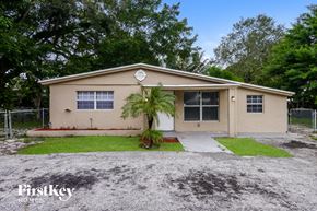 Hollywood house for rent - A small house with a brown roof and tan walls is surrounded by a gravel driveway and a grassy area.