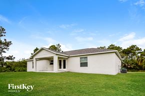 Englewood house for rent - A white house with a brown roof is surrounded by green grass.