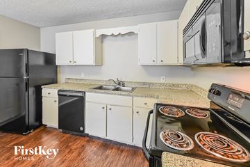 Houston house for rent - A kitchen with a black fridge, white cabinets, and a stove top oven.