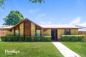 Garland house for rent - A house with a brown door and windows is surrounded by green bushes.