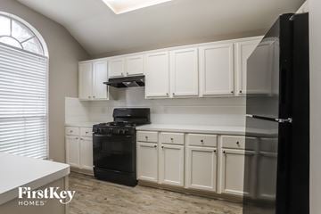 Katy house for rent - a kitchen with white cabinets and a black stove and refrigerator